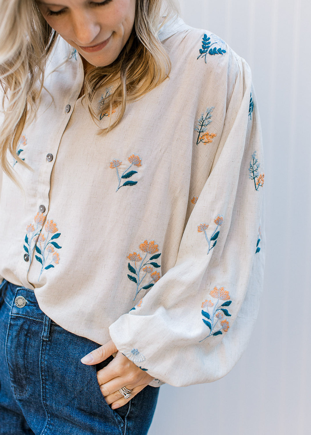 Close up of bubble long sleeve on an oatmeal button up with embroidered blue and yellow floral. 