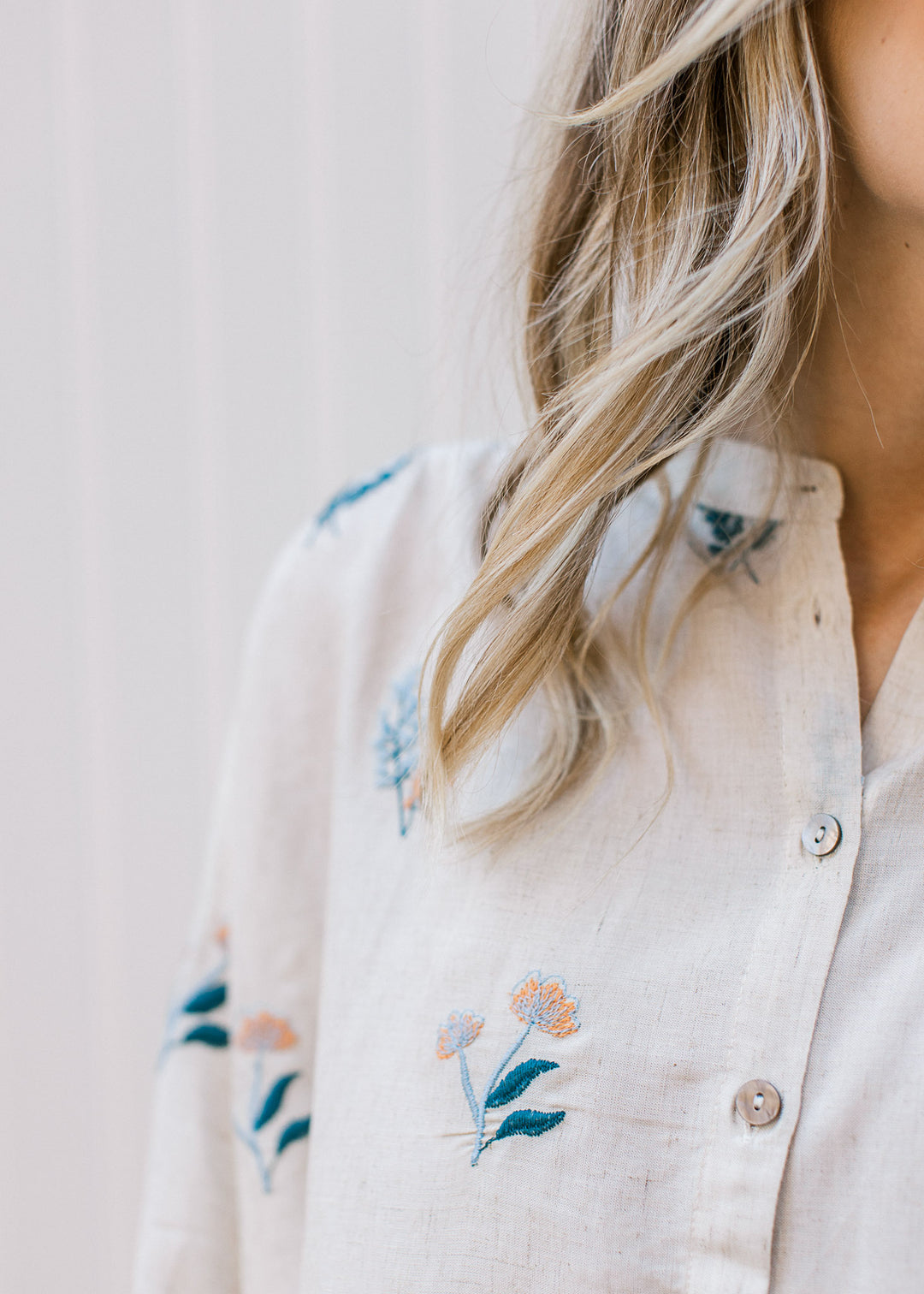 Close up of yellow and blue embroidered floral on an oatmeal button up top with long bubble sleeves.
