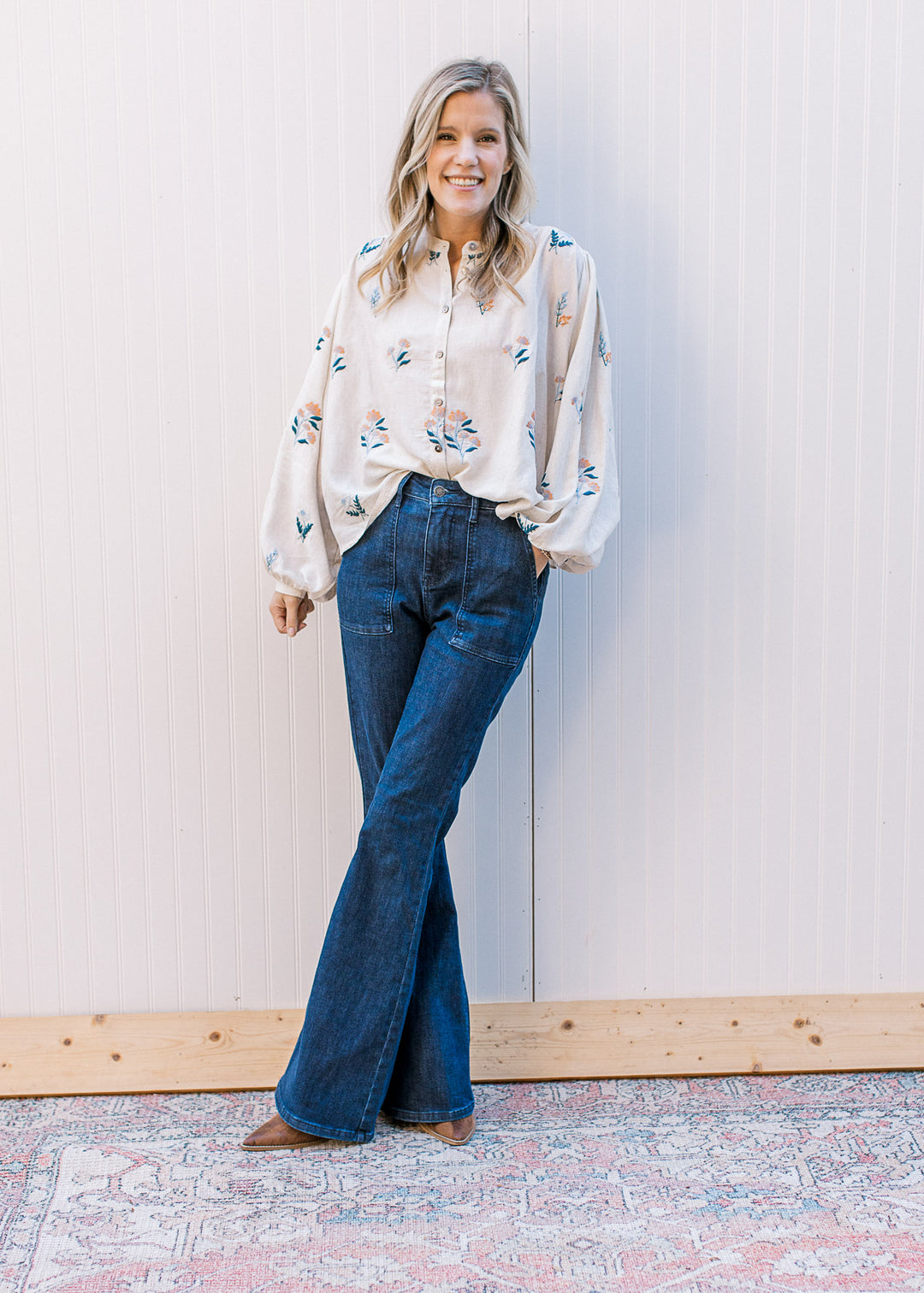 Model wearing jeans, boots and an oatmeal button up with blue and golden flowers. 