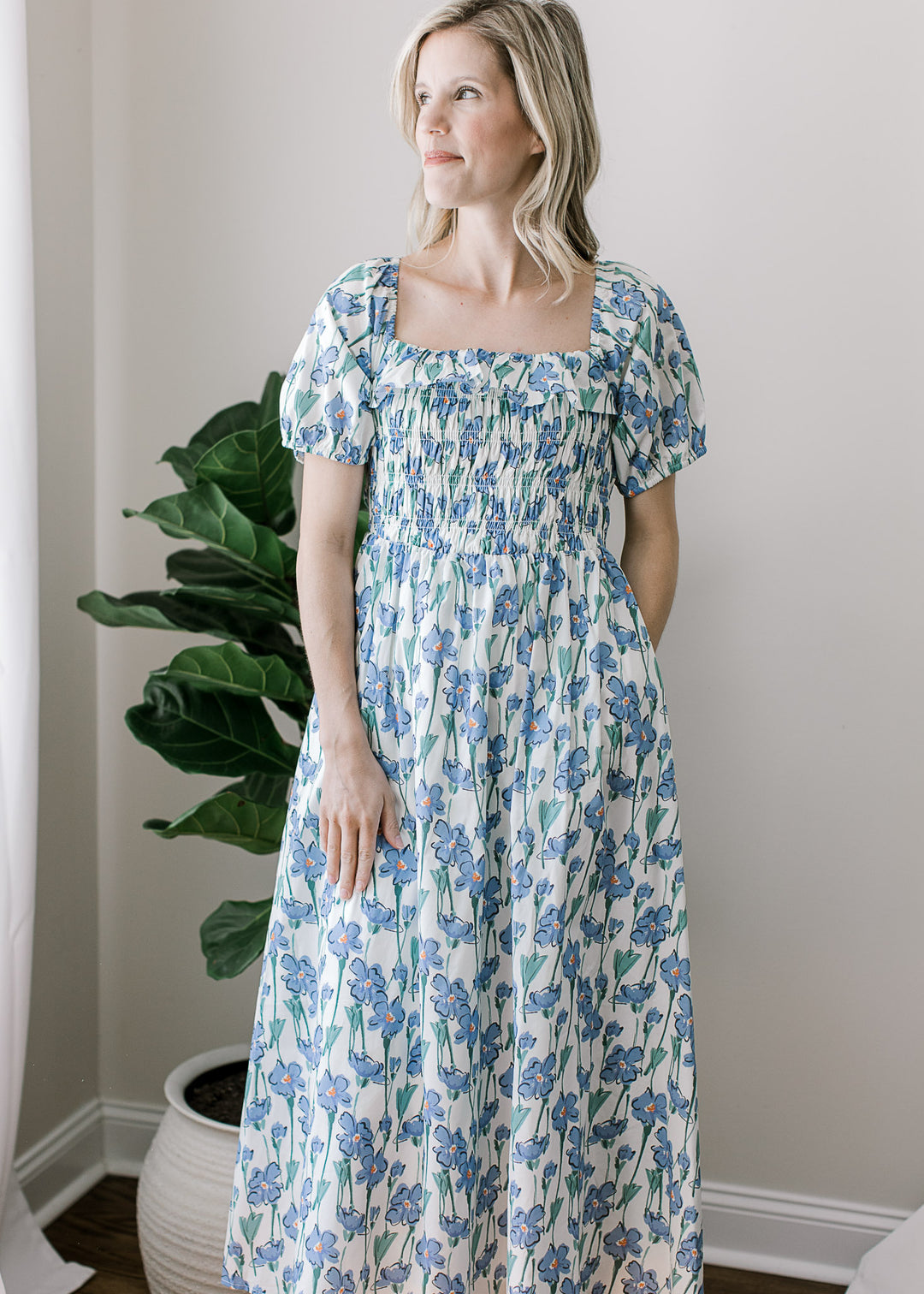 Model wearing a cream midi with blue floral, bubble short sleeves, pockets, and smocked bodice.