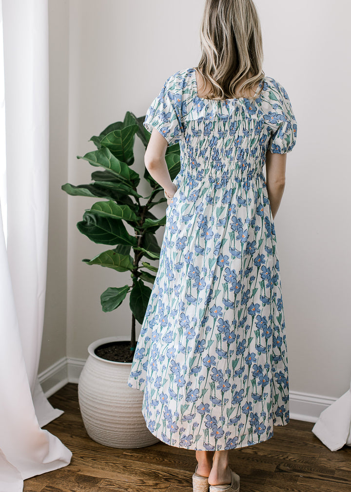 Back view of Model in a cream midi with blue floral, short sleeves, square neck and smocked bodice.
