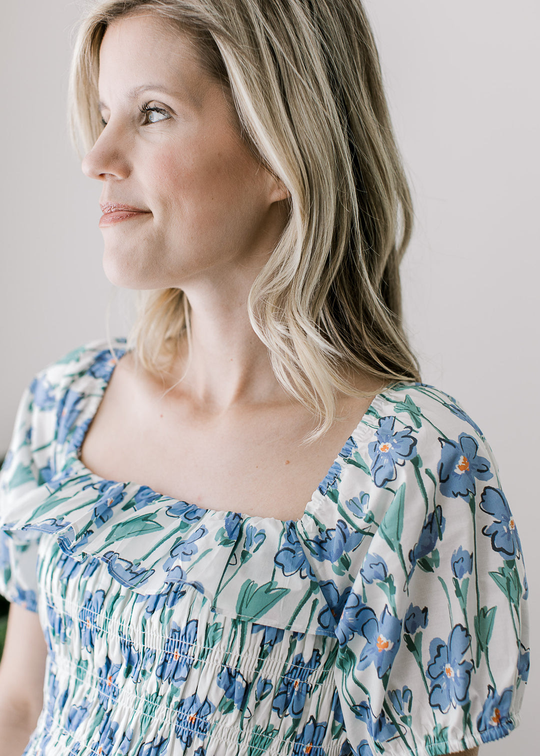 Close up of square neckline with ruffle on a cream midi with blue floral and a smocke bodice. 