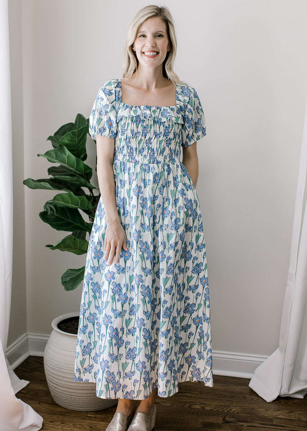 Model wearing heels and a cream midi with blue floral, square neck and smocked bodice.