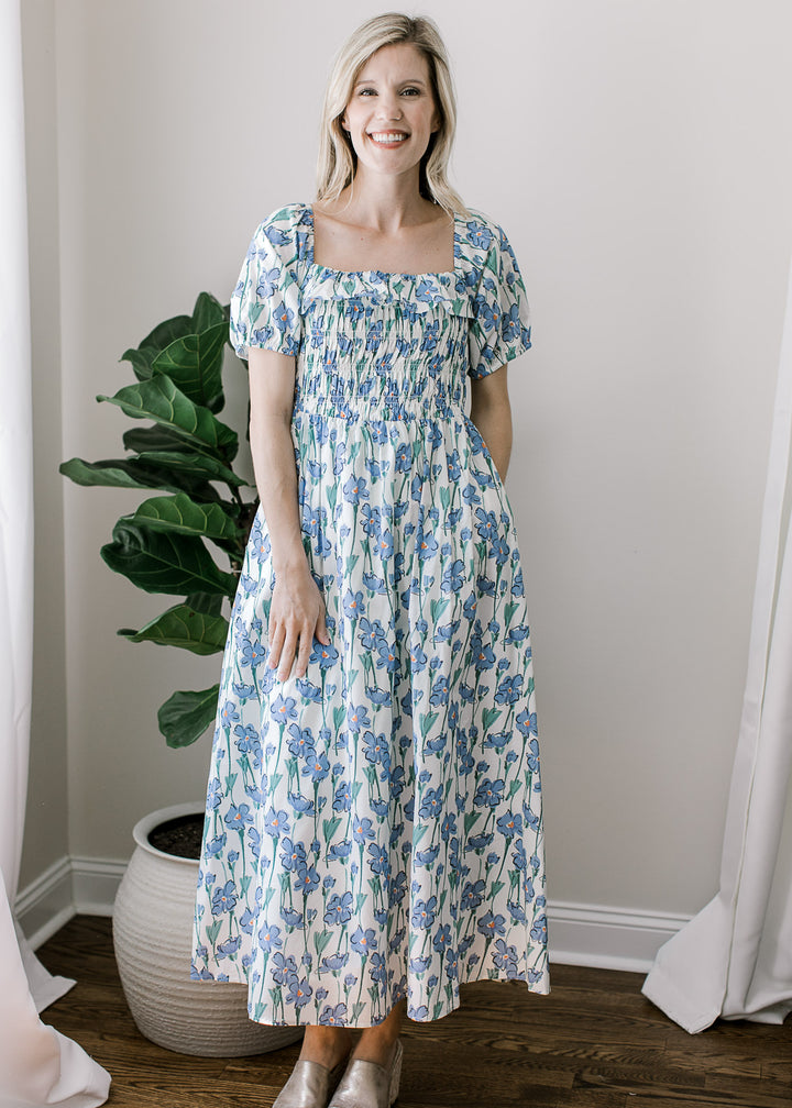 Model wearing heels and a cream midi with blue floral, square neck and smocked bodice.