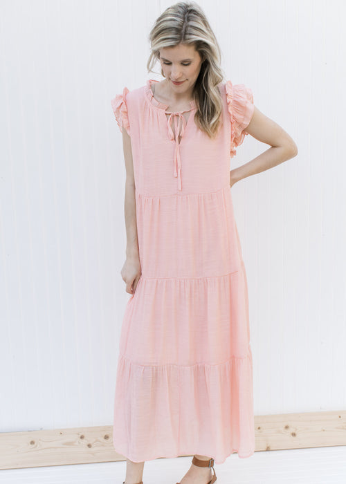 Model wearing a blush tiered midi with ruffle cap sleeves and v-neck with a tie.