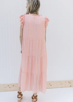 Back view of Model wearing a blush tiered midi with ruffle cap sleeves and v-neck with a tie.