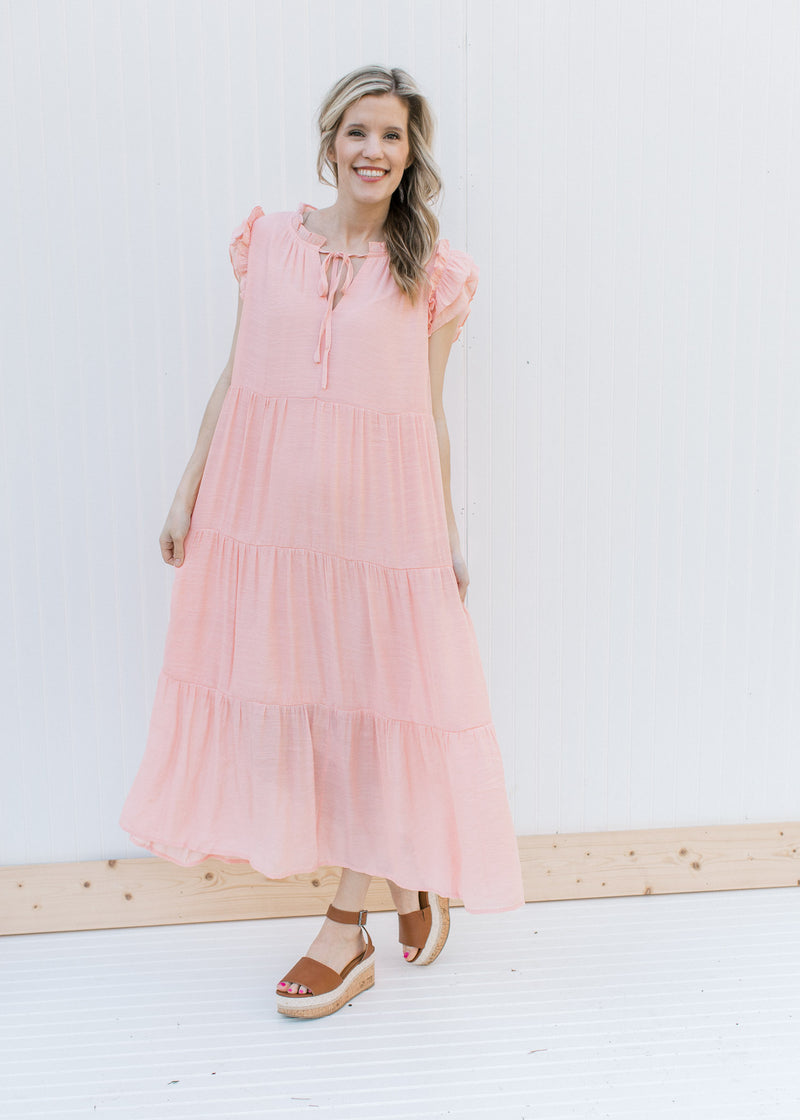 Model wearing heels with a blush tiered midi with ruffle cap sleeves and v-neck with a tie.