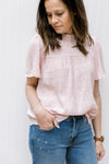 Close up of the textured material on a blush top with a ruffled mock neck and short sleeves.