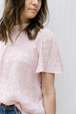 Close up of textured material on the short sleeve of a blush top with a ruffle detail at neck