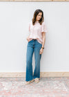 Model wearing jeans, sandals and a textured blush top with a ruffled neck and short sleeves.