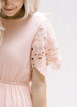Close up view of lace short sleeves with scalloped edge on a model wearing a pale pink dress. 