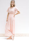 Model in a pale pink maxi dress with an elastic waist and lace short sleeves with scalloped edge. 