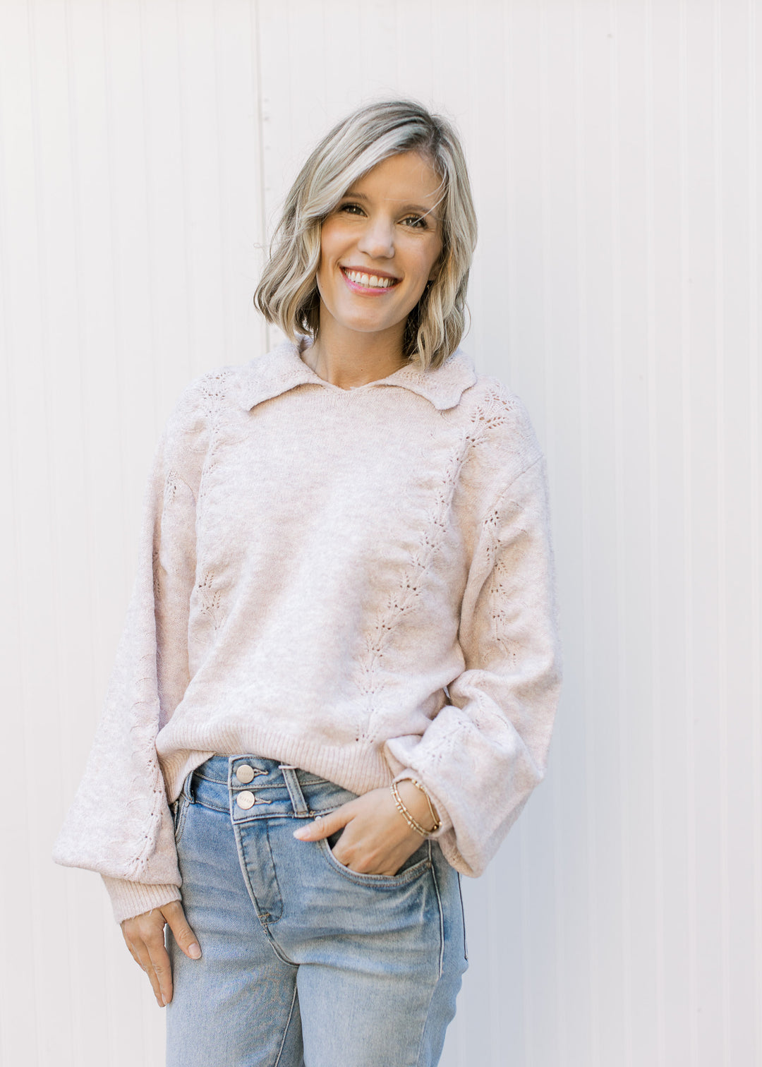 Model wearing a soft blush sweater with scalloped flap collar, long bubble sleeves and knit detail. 