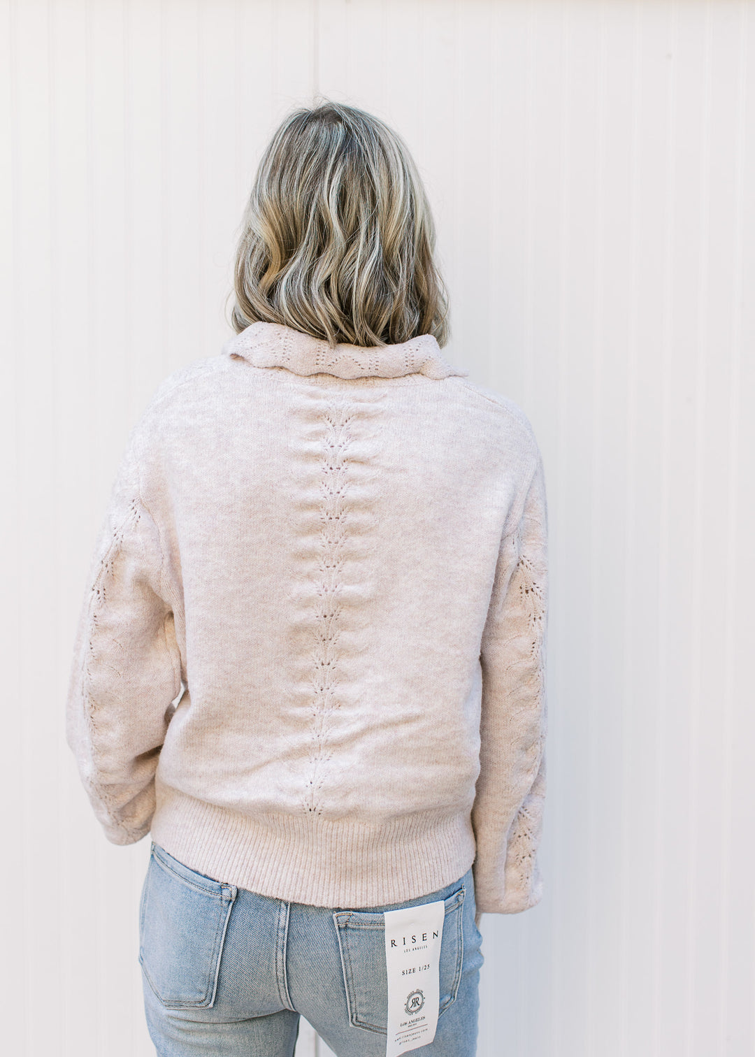 Back view of Model wearing a soft blush sweater with scalloped flap collar and long sleeves. 