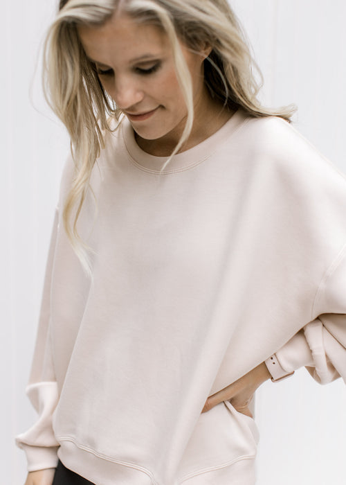 Model wearing a blush slightly cropped sweatshirt with long sleeves and a round neck. 