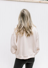 Back view of Model wearing a blush slightly cropped sweatshirt with long sleeves and a round neck. 