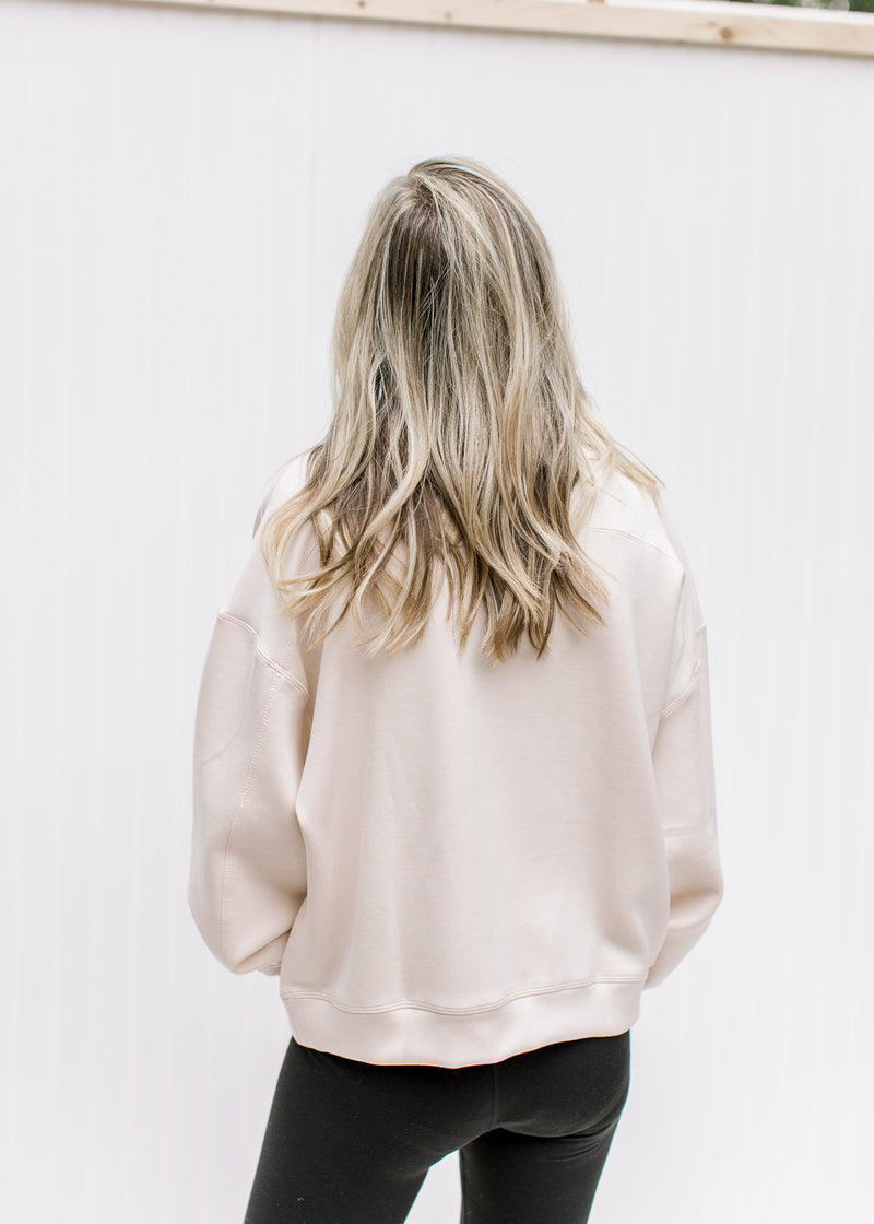 Back view of Model wearing a blush slightly cropped sweatshirt with long sleeves and a round neck. 