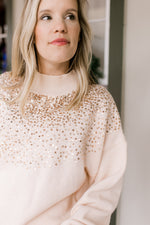 Model wearing a blush colored sweater with gold sequins at the mock neck and long sleeves. 