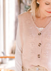 Close up of embroidered flowers v-neck and button front on a blush sweater vest. 