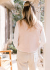 Back view of model wearing a blush sweater vest with embroidered flowers and button front. 