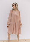 Model wearing a blush v-neck dress with long sleeves and tiers with a cross hem
