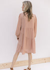 Back view of Model wearing a blush v-neck dress with long sleeves and tiers with a cross hem