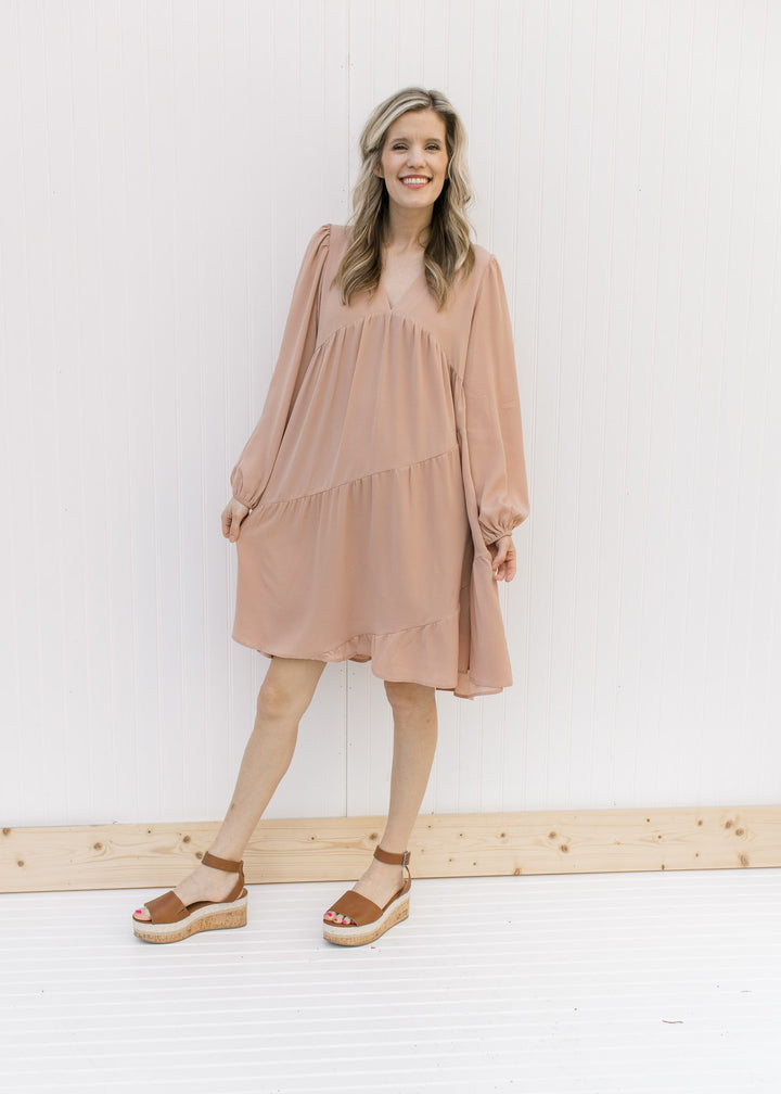 Model wearing heels with a blush v-neck dress with long sleeves and tiers with a cross hem 
