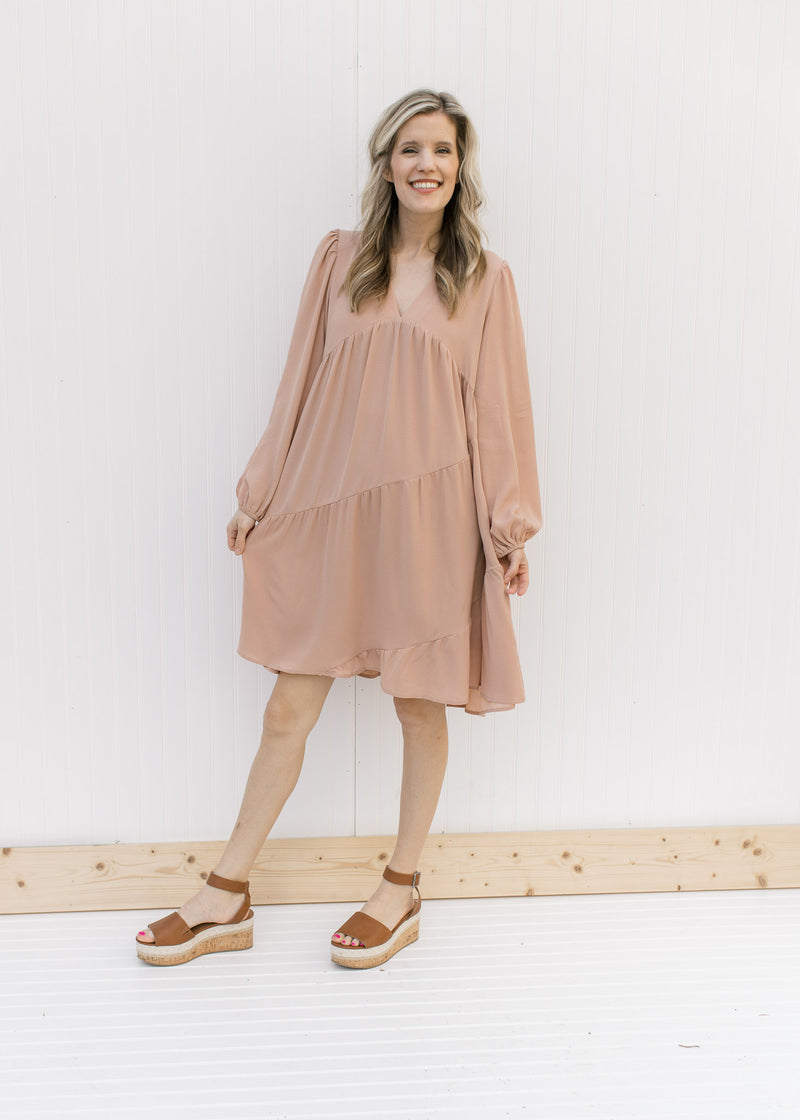 Model wearing heels with a blush v-neck dress with long sleeves and tiers with a cross hem 