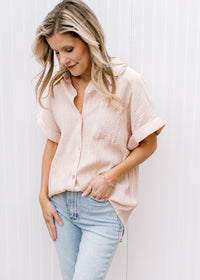 Model wearing a peach button up top with crinkle fabric, collar and short sleeves with a cuff.