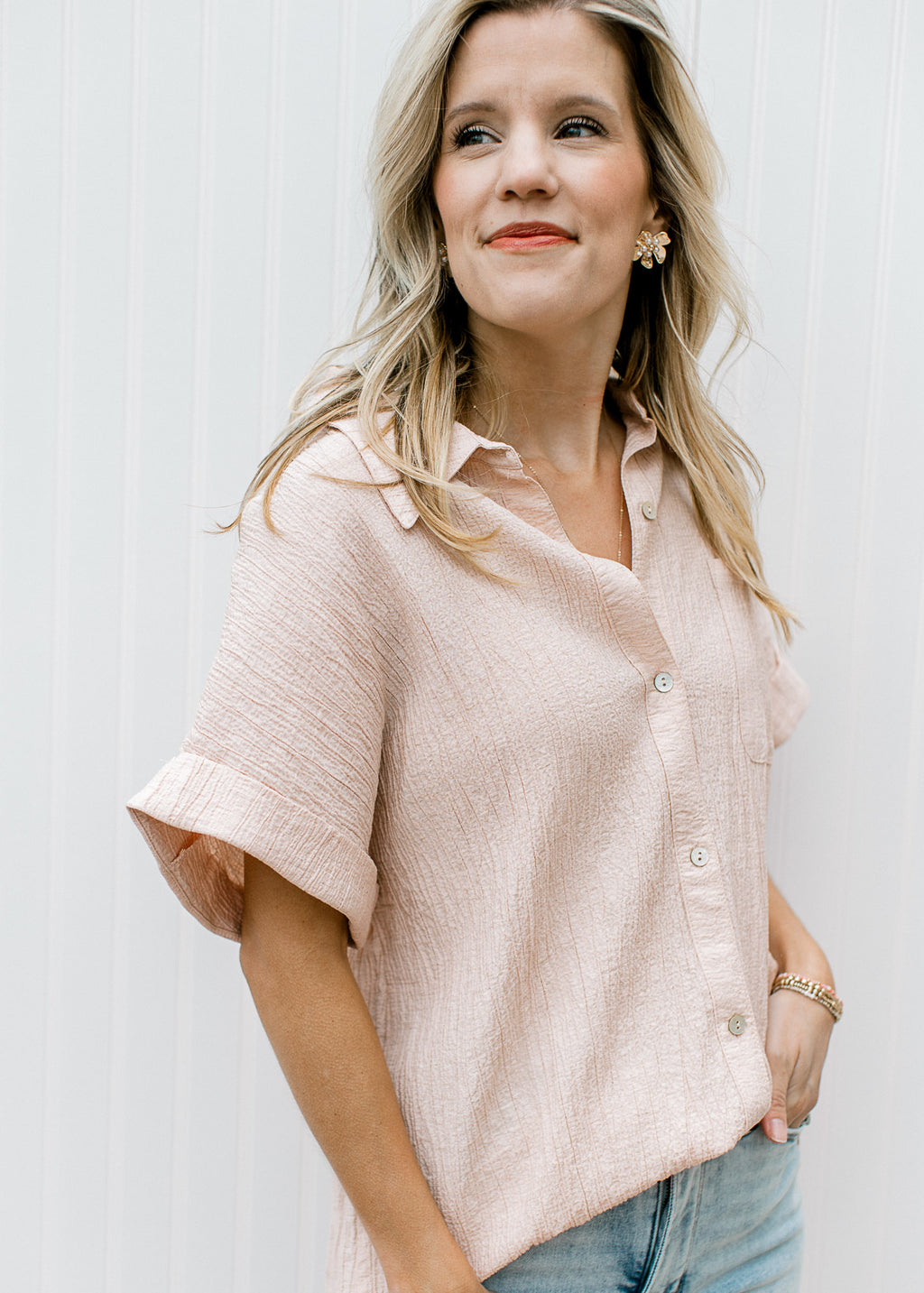 Side view of Model wearing a peach button up top with crinkle fabric and short sleeves with a cuff.