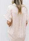 Back view of Model wearing a peach button up top with crinkle fabric and short sleeves with a cuff.