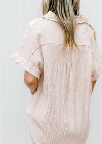 Back view of Model wearing a peach button up top with crinkle fabric and short sleeves with a cuff.