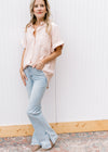 Model wearing jeans and a peach button up top with crinkle fabric short sleeves with a cuff.
