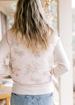 Back view of model wearing a pale pink puffer vest with  flowers, mock neck and pockets