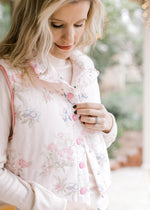 Model wearing a pale pink vest with  soft colored flowers, mock neck, pockets and snap closure. 