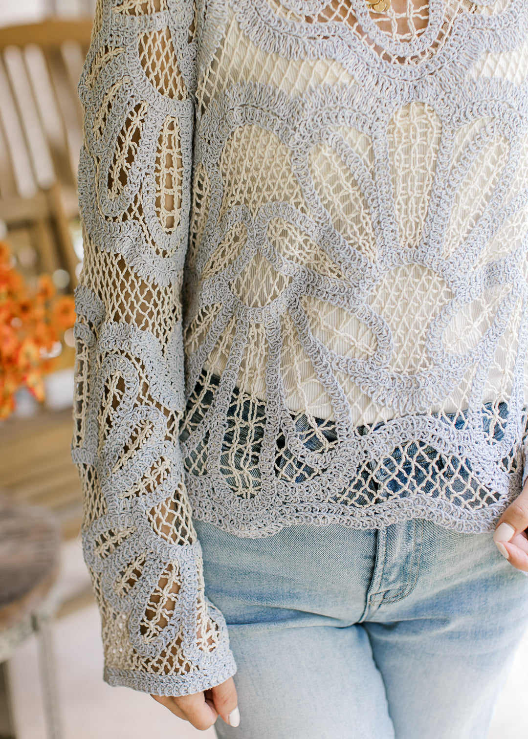 Close up of scalloped hem and bell long sleeves on a pale blue and cream open knit sweater. 