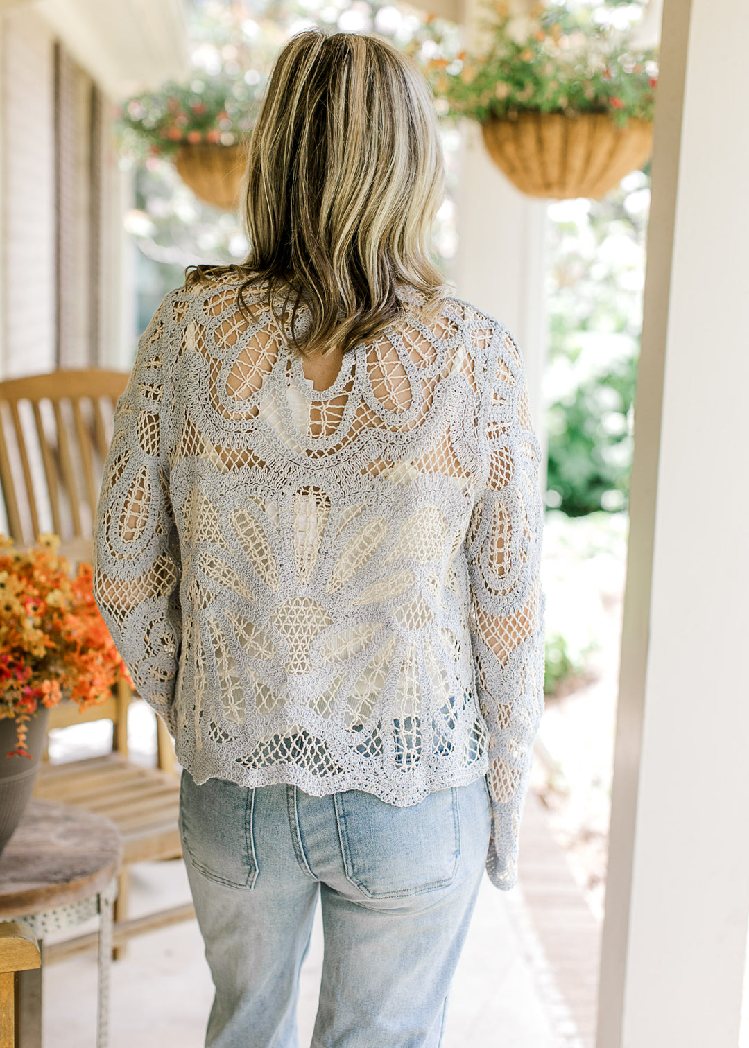 Back view of Model wearing a pale blue open knit sweater with a scallop hem and long sleeves.