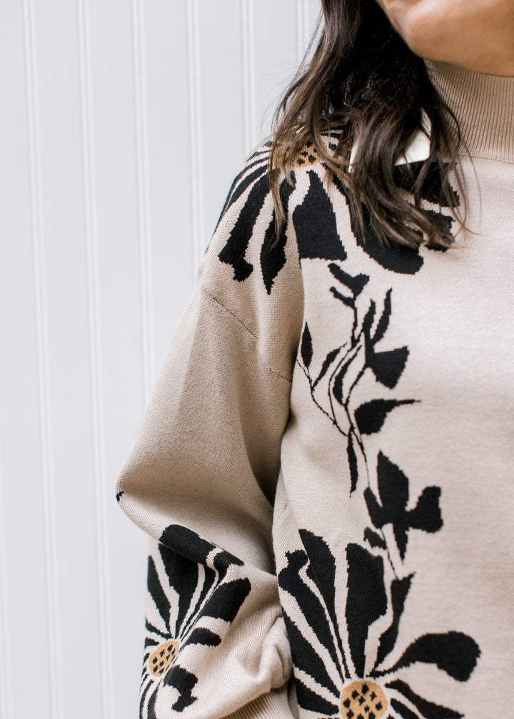 Close up of bold black floral pattern on a tan sweater with bubble long sleeves and a mock neck. 