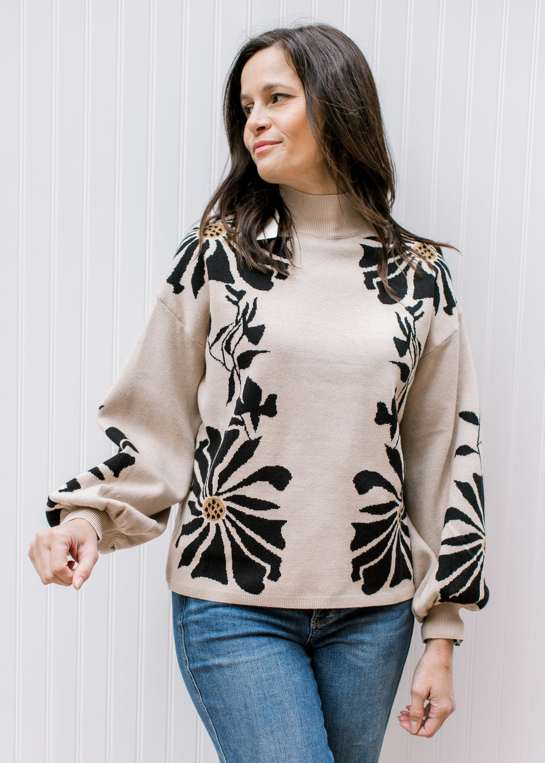 Model wearing jeans and a tan sweater with black floral pattern, a mock neck, and long sleeves. 