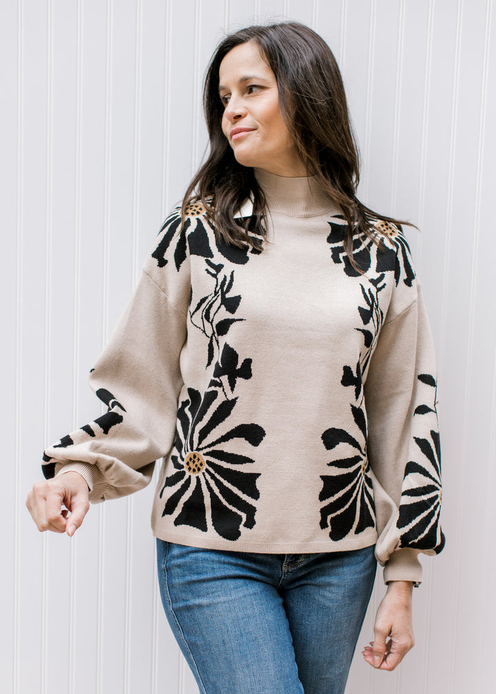 Model wearing jeans and a tan sweater with black floral pattern, a mock neck, and long sleeves. 
