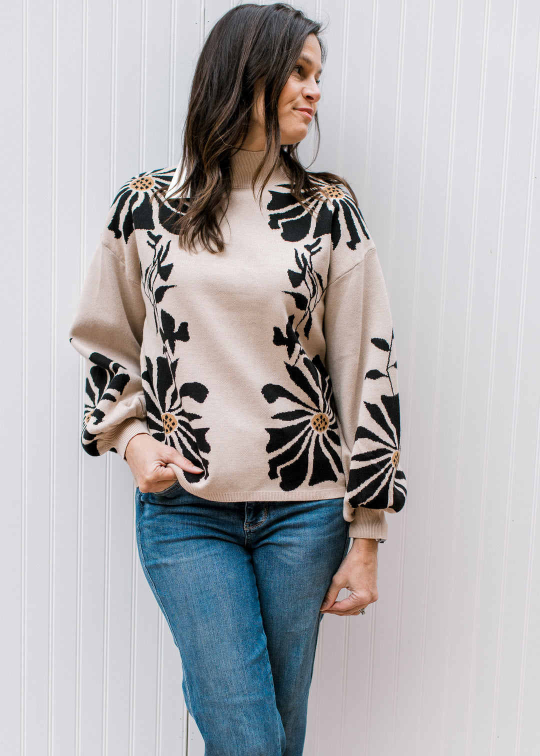 Model wearing a tan sweater with bold black floral pattern, a mock neck, and bubble long sleeves. 