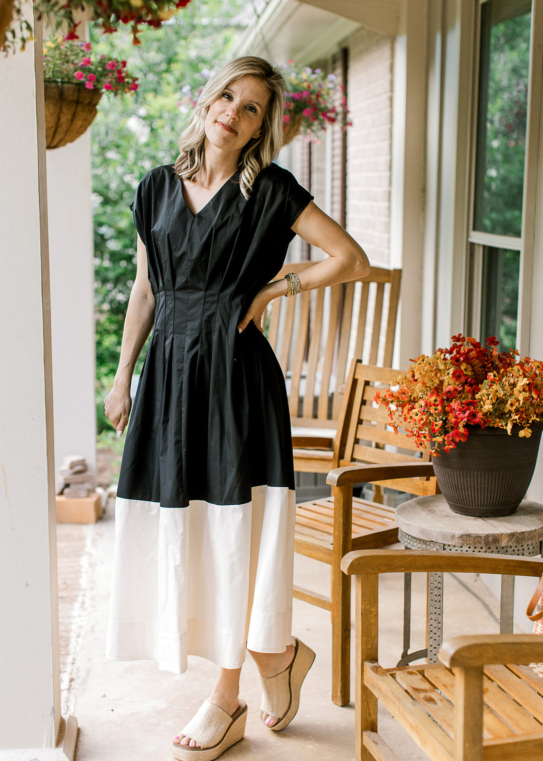Model wearing a black and cream v-neck midi with cap sleeves and pleating at the waist. 