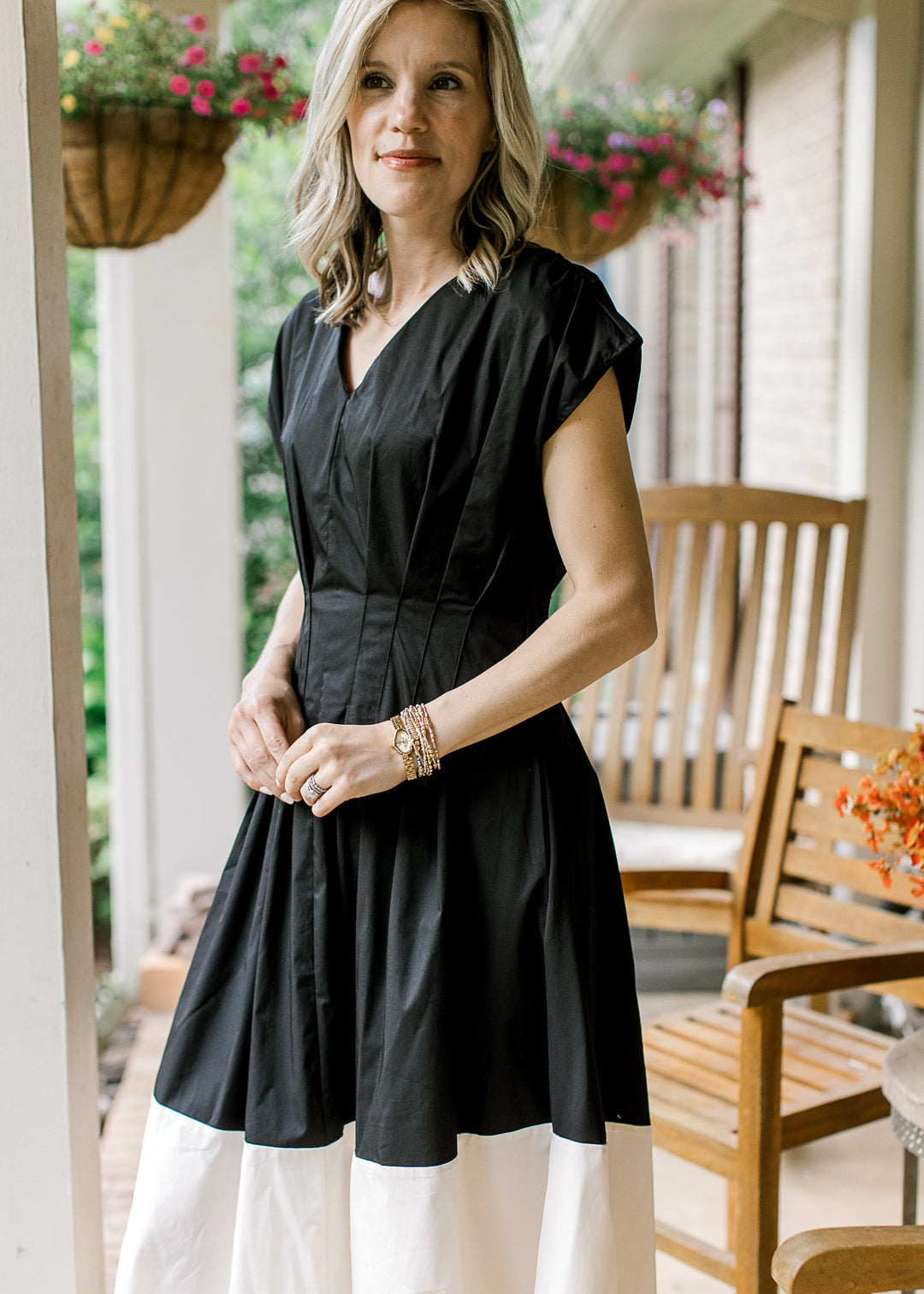 Model wearing a v-neck black and cream dress with pleating all around the waist and capped sleeves.