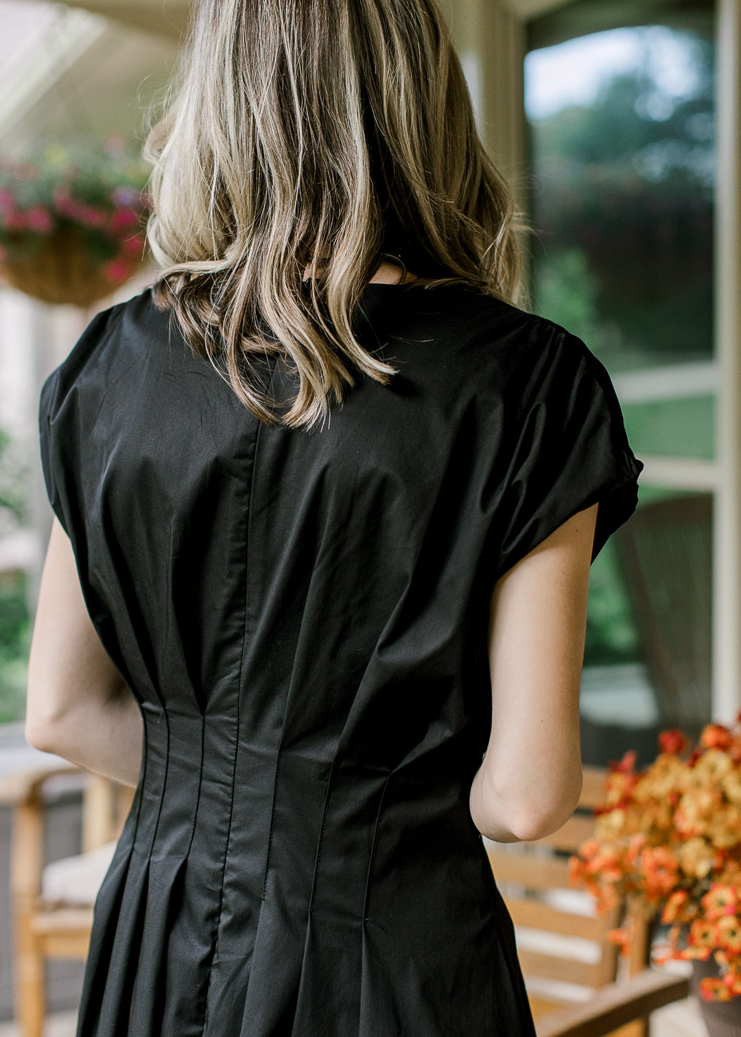 Back view of Model wearing a black and cream midi with cap sleeves and pleating around the waist. 