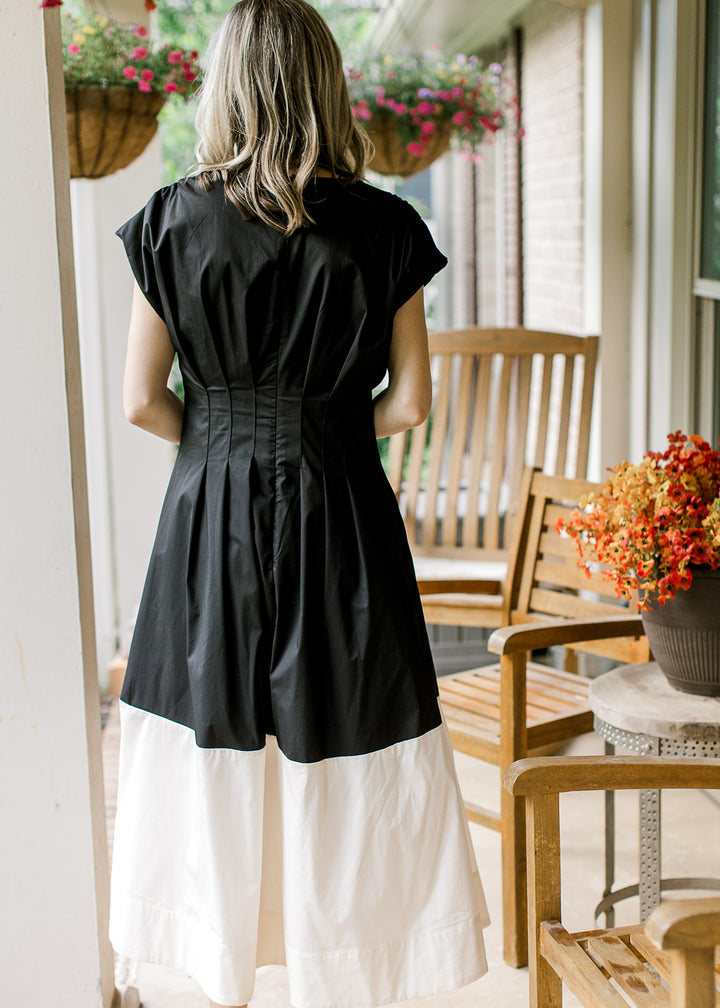 Back view of model wearing a black and cream colorblock midi with cap sleeves and pleated waist. 