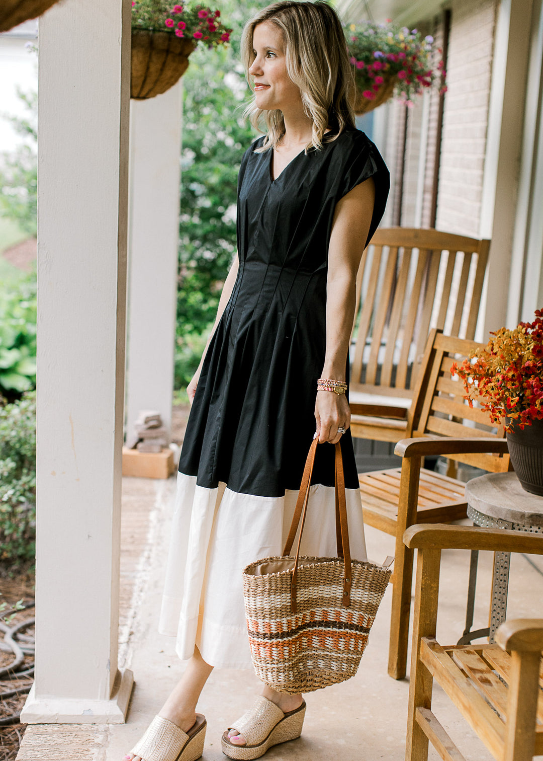 Model with a purse in a black and cream colorblock midi with cap sleeves and pleating at the waist. 