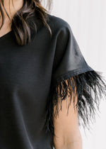 Close up of feather accent on the short sleeve of a black v-neck top. 
