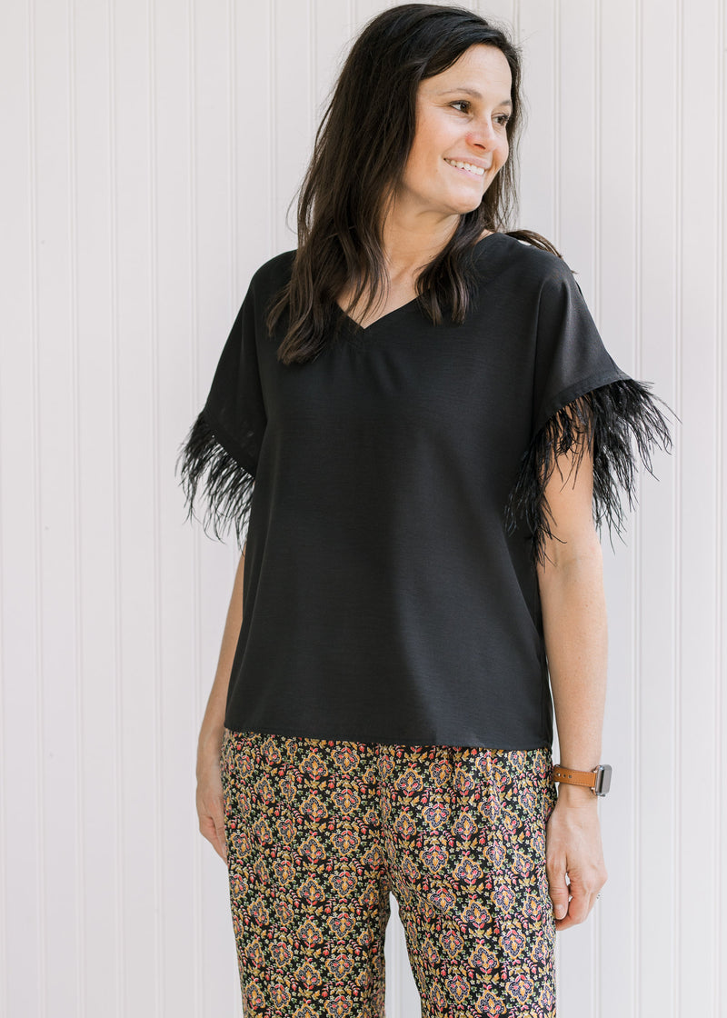 Model wearing a black v-neck top with a feather accent on the short sleeves. 