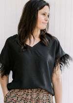 Model wearing a black polyester blend v-neck top with a feather accent on the short sleeves. 
