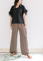 Model wearing black wide leg pants with a gold, rose and green pattern, elastic waist and pockets. 